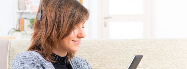 A female wearing a cochlear implant smiles at her digital tablet