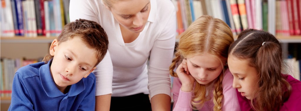 A teacher supports three primary school children in the classroom, by talking about learning